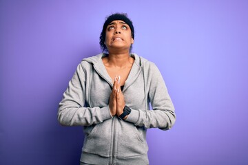 Young african american sportswoman doing sport wearing sportswear over purple background begging and praying with hands together with hope expression on face very emotional and worried. Begging.