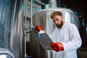 Caucasian male professional  technologist expert in white suit  operating production machine in food factory and doing quality control and holding checklist. Checking production in food industry.