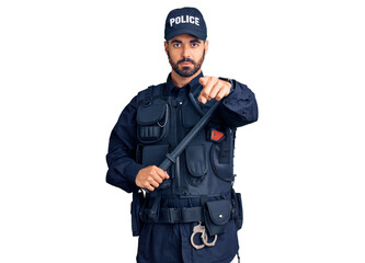 Young hispanic man wearing police uniform holding baton pointing with finger to the camera and to you, confident gesture looking serious