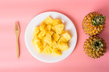 Sliced pineapple fruit on white plate with fork ready to eating on pastel pink background, Tropical fruit