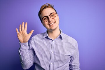 Young handsome redhead man wearing casual shirt and glasses over purple background showing and pointing up with fingers number five while smiling confident and happy.