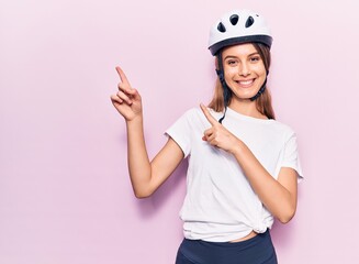 Young beautiful girl wearing bike helmet smiling and looking at the camera pointing with two hands and fingers to the side.