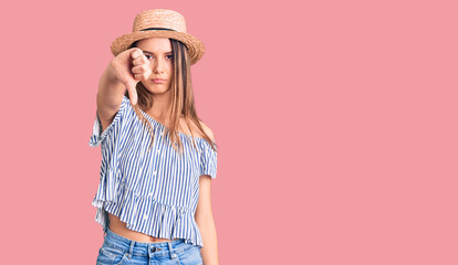 Young beautiful girl wearing hat and t shirt looking unhappy and angry showing rejection and negative with thumbs down gesture. bad expression.