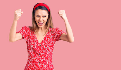 Young beautiful girl wearing dress and diadem angry and mad raising fists frustrated and furious...