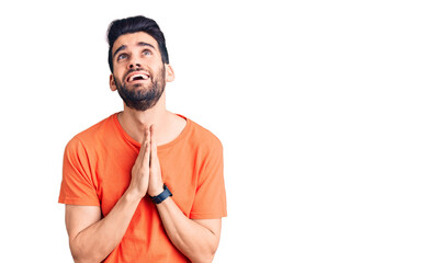 Young handsome man with beard wearing casual t-shirt begging and praying with hands together with hope expression on face very emotional and worried. begging.