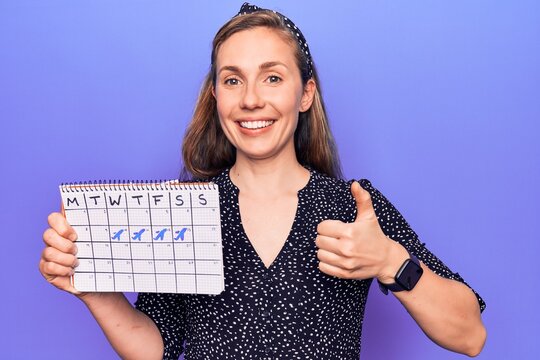 Young beautiful blonde woman holding holidays trip calendar smiling happy and positive, thumb up doing excellent and approval sign