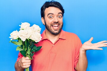 Young hispanic man holding flowers celebrating achievement with happy smile and winner expression with raised hand