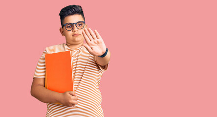 Little boy kid holding book wearing glasses doing stop sing with palm of the hand. warning...