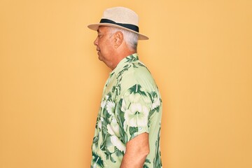 Middle age senior grey-haired man wearing summer hat and floral shirt on beach vacation looking to side, relax profile pose with natural face with confident smile.