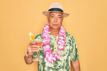 Middle age senior grey-haired man wearing summer hat and hawaiian lei drinking a cocktail with a confident expression on smart face thinking serious