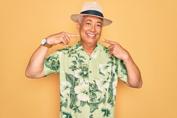 Middle age senior grey-haired man wearing summer hat and floral shirt on beach vacation smiling cheerful showing and pointing with fingers teeth and mouth. Dental health concept.