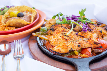 A view of chicken fajitas served in a skillet, with a side of rice and beans, in a restaurant or kitchen setting.