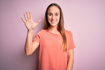 Young beautiful woman wearing casual t-shirt standing over isolated pink background showing and pointing up with fingers number five while smiling confident and happy.