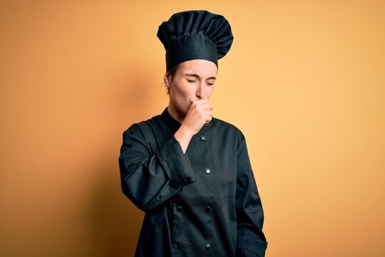 Young beautiful chef woman wearing cooker uniform and hat standing over yellow background feeling unwell and coughing as symptom for cold or bronchitis. Health care concept.