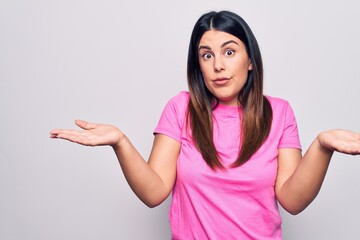 Young beautiful brunette woman wearing casual pink t-shirt standing over white background clueless...