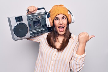Young beautiful brunette woman listening to music using vintage boombox and headphones pointing...