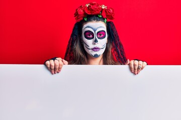 Young woman wearing day of the dead costume holding blank empty banner thinking attitude and sober expression looking self confident
