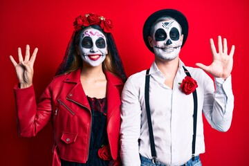 Couple wearing day of the dead costume over red showing and pointing up with fingers number nine while smiling confident and happy.