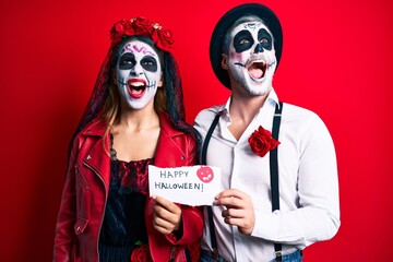 Couple wearing day of the dead costume holding happy halloween paper angry and mad screaming...