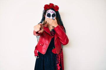 Woman wearing day of the dead costume over white laughing at you, pointing finger to the camera with hand over mouth, shame expression