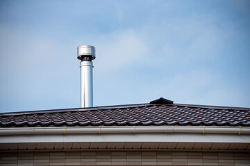 House roof with modern red metal tiles and steel chimney