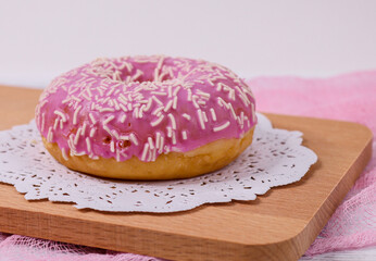 American donut with pink cream on a wooden board, close-up side view.