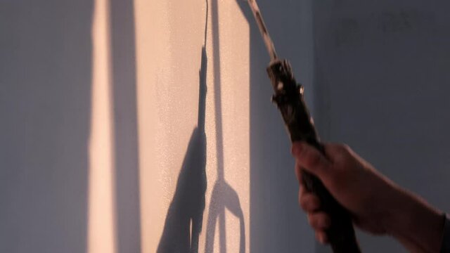 Slow motion close-up painting on a crisp white wall in the evening sun with the silhouette of a step ladder and a large paint roller and decorator in authentic painting attire