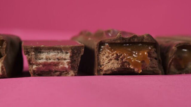 Tasty bitten chocolate candy bars slider move on pink background isolate. Unhealthy food for children and all people.