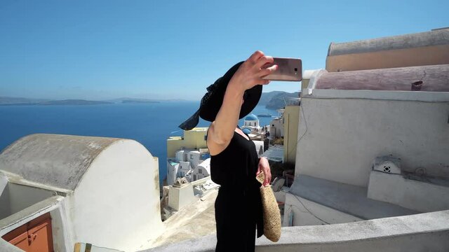 Fashion model making selfie on vacation to Oia, Santorini over white traditional house and churches architecture