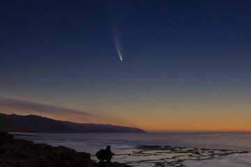 Fototapeta na wymiar Comet Neowise at dawn over coastal tide pools in the foreground and wisps of clouds over the mountains.