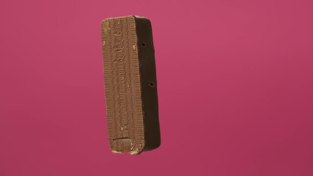 A delicious and unhealthy chocolate bar rotates on a pink background. Bitten sweets isolated. The unpacked bar is spinning. Nougat and caramel inside candy bar chocolate