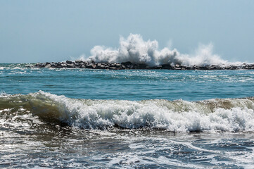 sea waves crashing against a breakwater in front of the beach