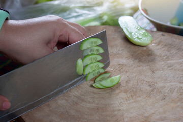 Hand of woman holding a knife to cut cucumber into slices on the butcher in the kitchen.