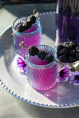 Servings of blackberry mocktails on a metal tray in bright sunlight.