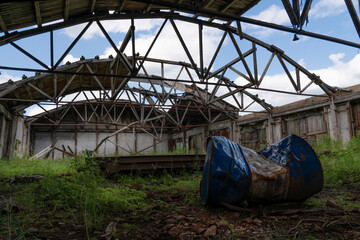 Obraz premium an old abandoned warehouse hangar with a ruined leaky roof and wooden floors, overgrown with grass inside. an old barrel in the foreground