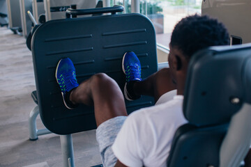 Back view of African American man doing exercise on leg press during fitness training in modern gym.