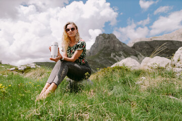 Naklejka na ściany i meble pretty woman holding tea mug and travel in mountains on vacations. Attractive woman drinks coffee and travel in mountains with beautiful summer view. National park of Durmitor, Montenegro. 