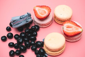 sweet round macaroons with daisies and blueberries on a pink background, top view