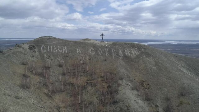 Orthodox cross on Mount Karabash. The camera flies away from them in the distance. The Title on the mountain: “Bless and save”. Russia, Chelyabinsk region
