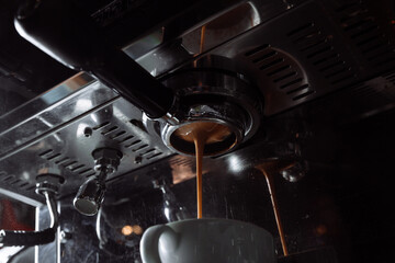 Preparation of espresso. Coffee pours from the coffee machine into the white cup. Professional coffee brewing.