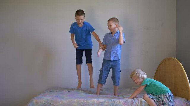 Three boys in shorts and T-shirts are jumping on bed. Children love to play together. Simple sports exercises at home