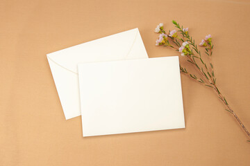 Envelope Mockup. Top view blank card on brown cloth background and wax flower.