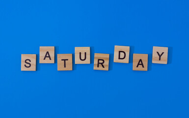 The word Saturday. Text day of the week in wooden letters.Black letters on wood, blue background with shadows. blank for design
