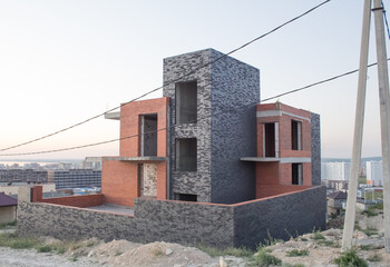  House under construction in a modern style from environmentally friendly materials. Unfinished two-story house of red and black brick without windows