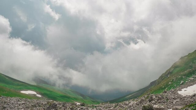 Beautiful panoramic shot of mysterious valley of the stunning Adygei mountains, covered with grass and stones under the huge clouds of sky in the Caucasus, Russia. Timelapse in nature with landscape.