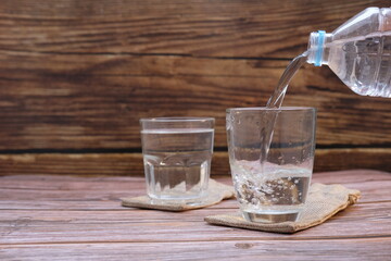 Pouring drinking water in glasses on wood table background and space for text