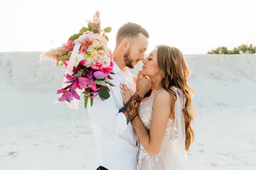 Love Story of a beautiful couple in a pink wedding luxury dress with a bouquet in the Sahara...