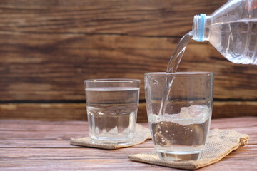 Pouring drinking water in glasses on wood table background and space for text