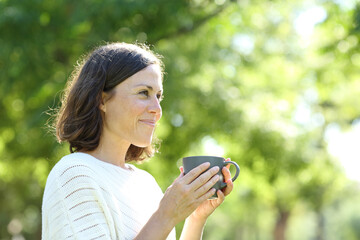Satisfied adult woman holding a coffee cup in the park