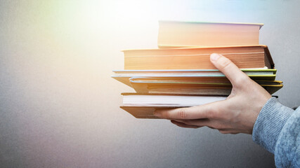 A large stack of books in the hands of a man. Self-study of a student, reading books